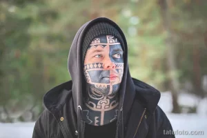 Фото экстремальной татуировки на лице в стиле трайбл. Черно-серый рисунок с геометрическими узорами, покрывающий большую часть лица.