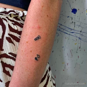 Фото тату: два небольших черных символа на запястье. Один символ похож на три соединенные окружности, другой - на сердце с линией.