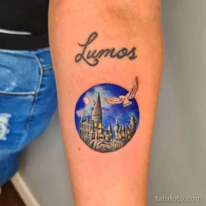 Фото тату с изображением Хогвартса и надписи 'Lumos'. Красочный рисунок татуировки, посвященный Гарри Поттеру, расположенный на руке.