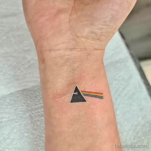 Фото тату с изображением логотипа группы Pink Floyd (треугольник и радуга) на запястье. Рисунок выполнен в ярких цветах.