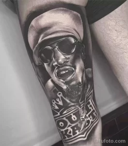 Фото тату 2Pac на руке в стиле реализм. Черно-белый портрет рэпера с солнцезащитными очками и надписью 'Thug Life'.