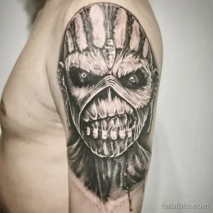 Фото тату: детализированный череп в стиле обложки альбома Iron Maiden, выполненный в черно-серых тонах на плече, с капающими кровью.