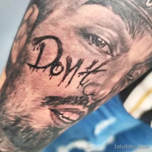 Фото тату надписи 'Don't' на фоне портрета на лице. Черно-серая татуировка с эффектом капающей краски и реалистичными деталями.