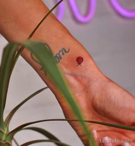 Фото татуировки божьей коровки на запястье. Маленькая, аккуратная татуировка с красным телом и черными точками, выполненная в минималистичном стиле.