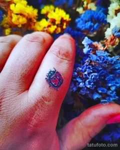 Фотография маленькой татуировки божьей коровки на пальце руки. Детализированный рисунок с яркими цветами.