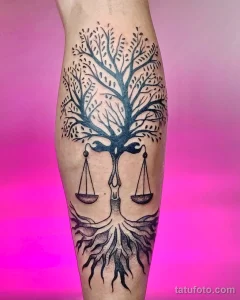 Фото тату Весы на икре, выполненное в технике blackwork. Изображение дерева с весами, символизирующее баланс и справедливость.