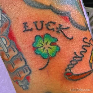 Фото тату на руке с изображением зеленого четырехлистного клевера и надписи 'LUCK' в черном цвете.