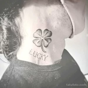 Фото тату на шее с изображением четырехлистного клевера и надписью 'LUCKY' в черном цвете.