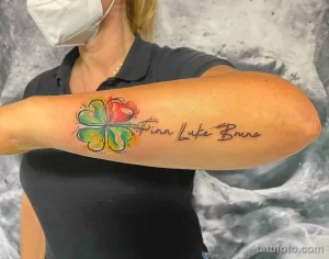 Фото тату на предплечье с изображением четырехлистного клевера и имен 'Finn Luke Bruno' в каллиграфическом стиле.