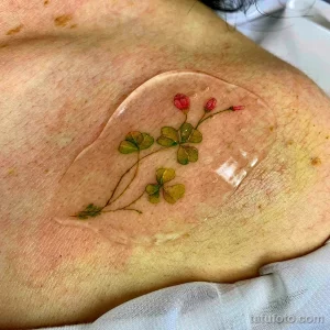 Фото нежной татуировки клевера и цветов на груди. Изящный рисунок татуировки с использованием пастельных тонов.