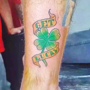 Фото тату клевера на ноге с надписью 'Get Lucky'. Яркий рисунок татуировки в стиле олдскул с зеленым клевером и красными акцентами.