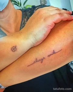 Фото тату: Пара татуировок на запястьях: маленький клевер и надпись 'always smile'. Минималистичный дизайн, выполненный тонкими линиями.