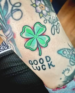 Фото тату клевера насыщенного зеленого цвета с надписью 'Good Luck' на руке. Детализированный рисунок татуировки, выполненный в ярком стиле.