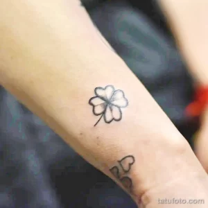 Фото тату: крошечный контурный рисунок четырехлистного клевера на внутренней стороне запястья, выполненный тонкими линиями.
