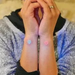 Фото тату: Яркие неоновые татуировки клевера и сердца на запястьях двух людей, выполненные в минималистичном стиле.