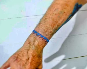 Фото тату: тонкий браслет с волнистыми линиями и небольшими элементами на запястье, выполненный в сине-красной гамме, минималистичный дизайн.