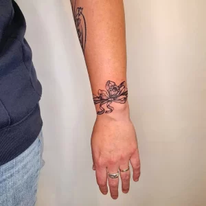 Фото тату: изящный рисунок цветка лотоса в стиле минимализм на женском запястье, выполненный тонкими черными линиями.