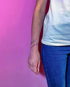 Фото татуировки с тонкой веточкой и листьями на запястье. Простой и элегантный дизайн в черном цвете.