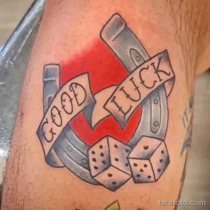 Фото татуировки подковы, костей и надписи 'Good Luck' на руке. Цветной рисунок, традиционный дизайн, удача и азарт.