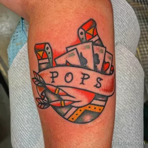 Фото тату в стиле олдскул на предплечье: карты, рюмка с напитком и надпись 'POPS'. Яркие цвета и четкие контуры.