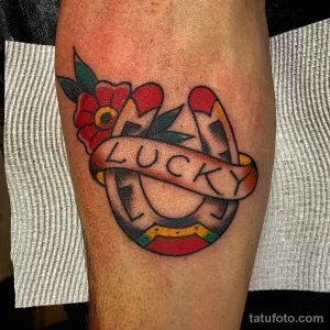 Фото тату подковы в стиле олд скул с надписью 'Lucky' на ленте. Яркий рисунок татуировки с использованием традиционных цветов.