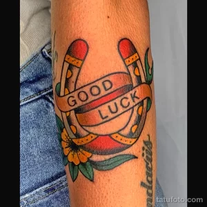 Фото тату подковы с надписью "Good Luck", выполненное в стиле олдскул на руке. Традиционный рисунок татуировки, символизирующий удачу и позитив.
