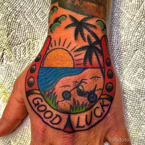 Фото тату на руке: цветная татуировка черепа в подкове с надписью 'Good Luck'. Традиционный стиль, яркие цвета, оригинальный дизайн.
