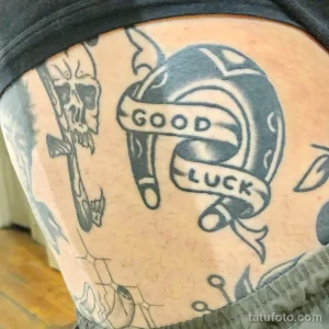 Фото тату подковы в стиле олд скул с надписью 'Good Luck' на руке. Черно-серый рисунок татуировки с четкими контурами и традиционным дизайном.