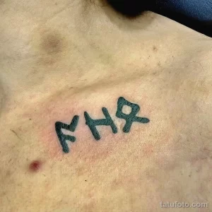 Фото тату: Небольшая татуировка на груди с изображением нескольких рунических символов, выполненных черными чернилами. Татуировка имеет простой и лаконичный дизайн.