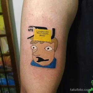 Фото тату мультяшного персонажа на плече. Яркий и забавный рисунок в стиле мультфильма с надписью. Идея для оригинальной татуировки.