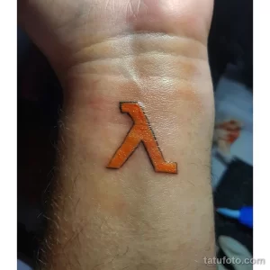 Фото минималистичного тату на запястье, изображающего символ Lambda из игры Half-Life. Простой и лаконичный дизайн.
