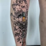 Фото тату в стиле blackwork на ноге. Черно-белый рисунок с цветами, ножом и глазом, детализированная проработка.