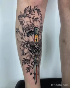 Фото тату в стиле blackwork на ноге. Черно-белый рисунок с цветами, ножом и глазом, детализированная проработка.