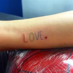 Фото тату на руке с надписью LOVE, выполненное простым шрифтом с добавлением маленького сердечка.