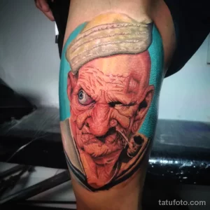 Фото тату реалистичного портрета пожилого мужчины с трубкой на мужском бедре. Рисунок выполнен в ярких цветах с использованием теней и бликов.