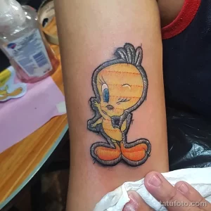 Фото тату на руке: мультяшный персонаж Твити из Looney Tunes с большими глазами и желтым оперением. Нежный и забавный рисунок.