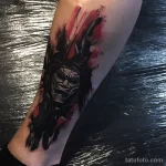 Фото тату с изображением маски, выполненной в стиле blackwork с использованием черных чернил и эффекта брызг.