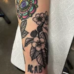Фото татуировки с изображением цветка, глазного яблока и надписи "ACAB" на руке. Необычный и провокационный рисунок.