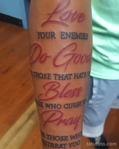 Фото тату на предплечье: надпись "Love Your Enemies, Do Good, Bless, Pray" в каллиграфическом стиле.