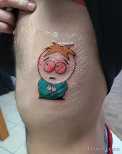 Фото татуировки с изображением Картмана из мультсериала South Park на бедре. Яркий, мультяшный стиль, выполненный в цвете.