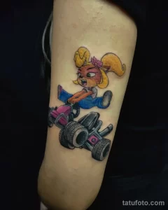 Фото татуировки Crash Bandicoot, едущего на карте, на предплечье. Изображение выполнено в ярких цветах в стиле мультфильма.