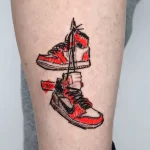 Фото татуировки на ноге. Изображены два кроссовка Nike, выполненные в ярких красных и черных тонах, с реалистичными деталями.