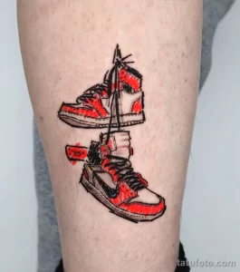 Фото татуировки на ноге. Изображены два кроссовка Nike, выполненные в ярких красных и черных тонах, с реалистичными деталями.
