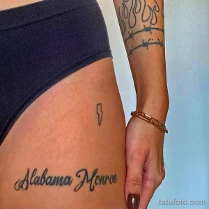 Фото тату с надписью 'Alabama Monroe' на бедре и изображением бритвы. Стильный рисунок татуировки в шрифтовом стиле.