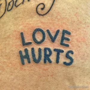 Фото тату с надписью 'Love Hurts' синим цветом на коже. Минималистичный рисунок татуировки, выполненный простым шрифтом.