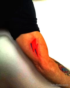 Фото тату с изображением красной молнии, выполненное в минималистичном стиле. Небольшой рисунок на лодыжке, символизирующий энергию и силу.