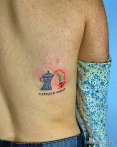 Фото татуировки на боку. Изображение кофеварки и радуги с надписью "Coffee & Perreo", выполненное в ярких цветах.