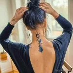 Фото тату: тонкая ветка с синими цветами, спускающаяся по затылку девушки. Минималистичный рисунок татуировки, выполненный в акварельной технике.