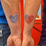 Фотография парных татуировок: два отпечатка пальцев, стилизованных под форму сердца, выполненных в синем и красном цветах.
