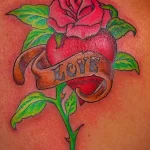 Фото тату на плече: красная роза обвивает сердце с надписью 'Love', выполненная в традиционном стиле с четкими контурами.
